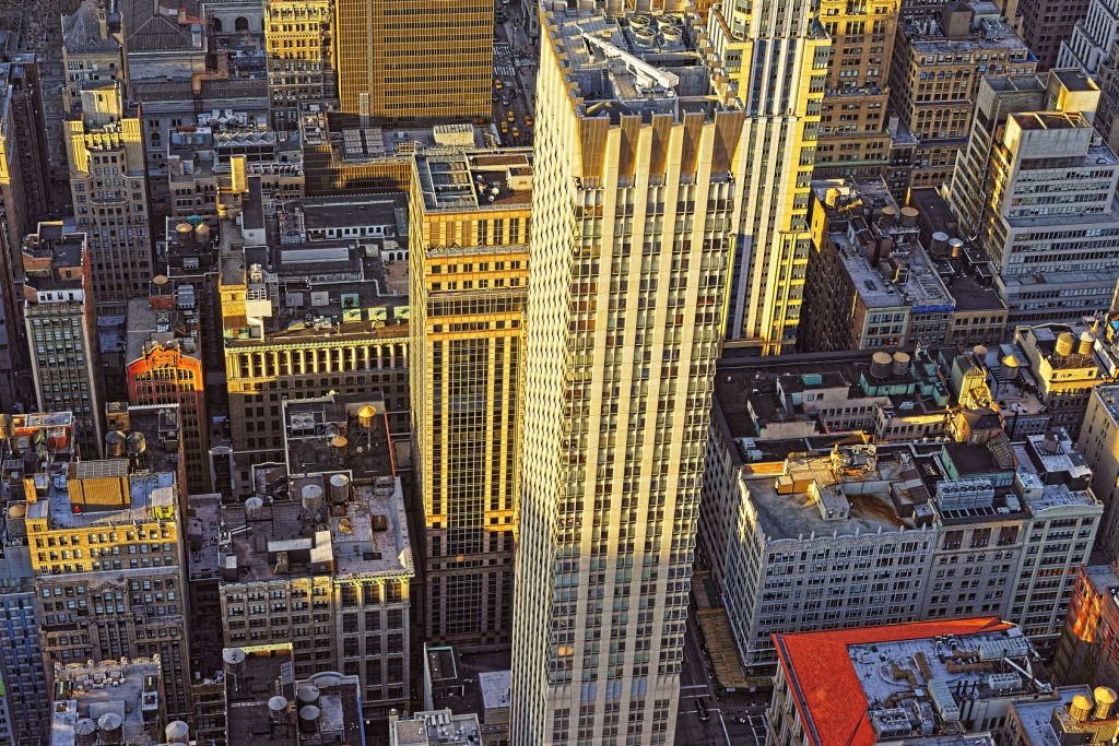 Aerial view from Empire State Building on Skyscrapers in Manhattan, New York, USA, at sunset. Most buildings look grey without sun. But roofs of the highest ones are lightened with sun and look golden